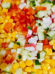 Red bell pepper, canned corn, cucumbers and crab meat are sliced for salad.