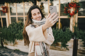 Young woman standing on festive decorated street, using her smartphone.