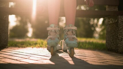 Leg view of individual seated outdoors in roller skates tapping ground with warm sunlight illuminating from behind, greenery visible in background