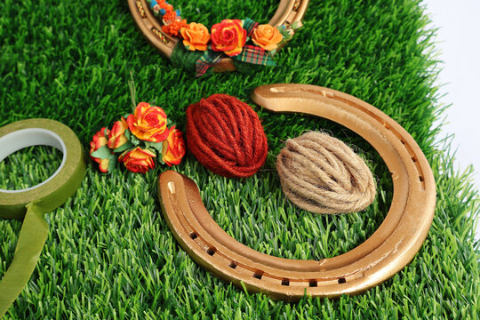 Horseshoe has been used and spray painted gold. Rolls of red, brown hemp rope, artificial flowers and a roll of green masking tape All placed on artificial grass.