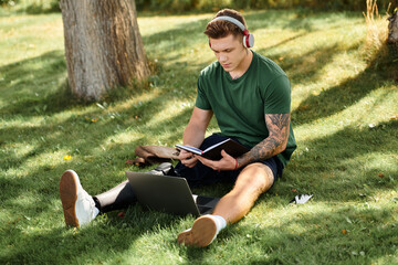 Obraz premium A young man with a prosthetic leg sits on the grass, focused on his notebook while enjoying the outdoor sun.