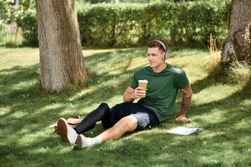 A young, handsome man sits comfortably on the grass with his prosthetic leg, sipping coffee and...
