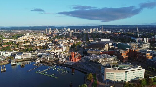 Aerial drone footage of Cardiff Bay area at sunrise, with the Cardiff city centre skyline visible in the distance. Slow straight descending shot.