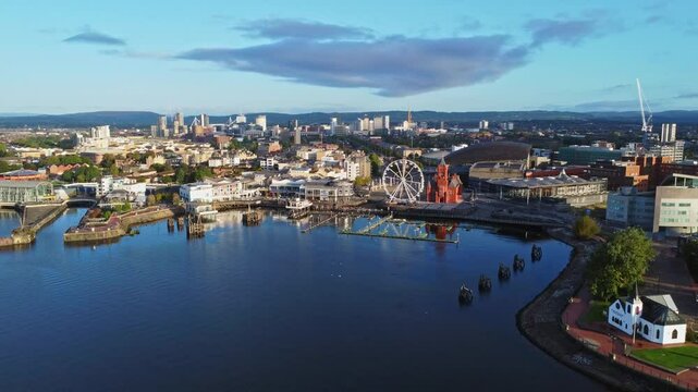 Aerial drone footage of Cardiff Bay area at sunrise, with the Cardiff city centre skyline visible in the distance. Diagonal ascending shot.