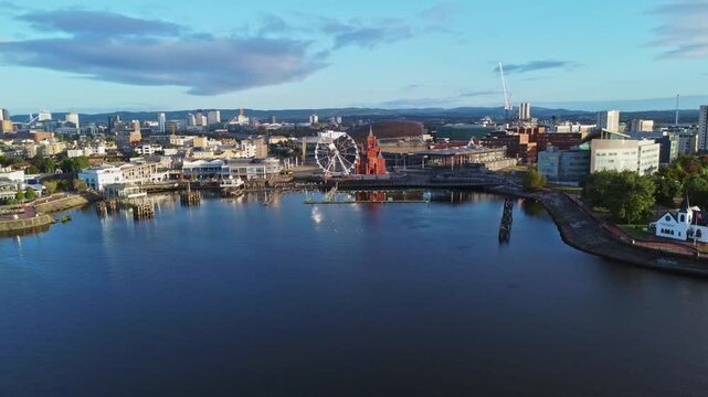 Aerial drone footage of Cardiff Bay area at sunrise, with the Cardiff city centre skyline visible in the distance. Mid altitude parallax, right-to-left tracking shot.