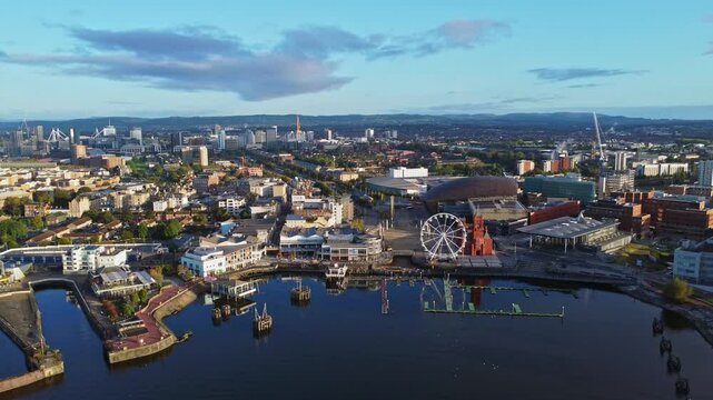 Aerial drone footage of Cardiff Bay area at sunrise, with the Cardiff city centre skyline visible in the distance. Diagonal descending shot.