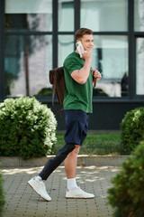 A young man with a prosthetic leg smiles while chatting on his phone in a lively outdoor scene.