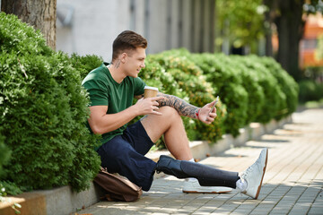 A young man with a prosthetic leg relaxes on a sunny day, sipping coffee and enjoying his...