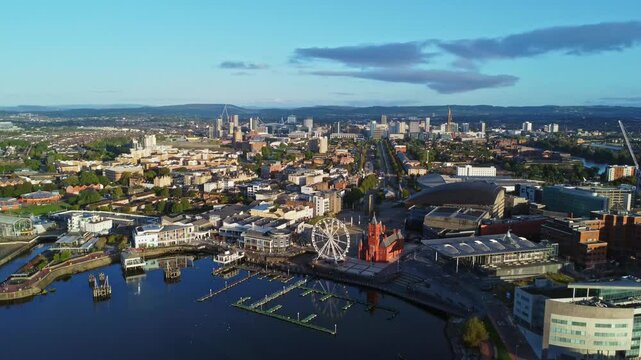 Aerial drone footage of Cardiff Bay area at sunrise, with the Cardiff city centre skyline visible in the distance. Revealing push-out shot with slow descent.