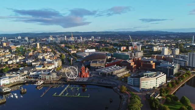 Aerial drone footage of Cardiff Bay area at sunrise, with the Cardiff city centre skyline visible in the distance. High altitude right-to-left tracking shot.