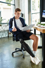 A young businessman with an artificial limb focuses on documents while seated at a stylish office desk.