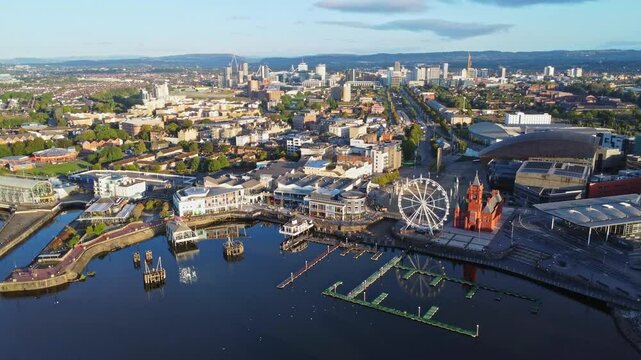 Aerial drone footage of Cardiff Bay area at sunrise, with the Cardiff city centre skyline visible in the distance. High angle pedestal up shot.