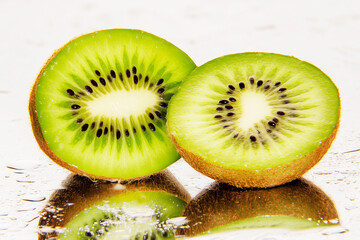 Two kiwi fruits are cut in half and placed on a table. The fruit is green and has black seeds, clean food.