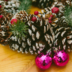 Wreath adorned with pine cones, red berries, and two shiny pink Christmas ornaments.