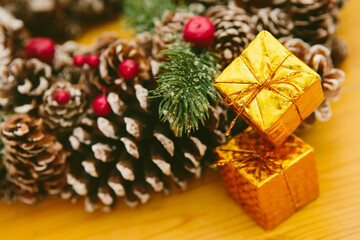 Two small golden gift boxes stacked, set against a blurred background of a festive Christmas wreath.