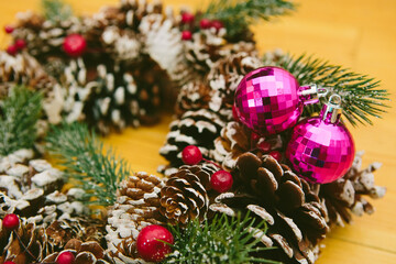 Wreath adorned with pine cones, red berries, and two shiny pink Christmas ornaments.