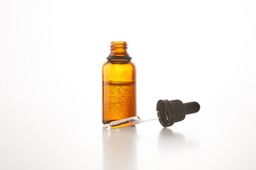 Black cap with pipette lies on open brown glass bottle.