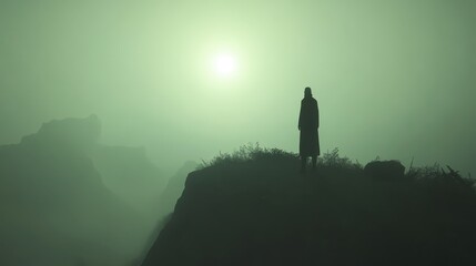 Fototapeta premium A lone figure stands on a misty cliff, silhouetted against a glowing sun, creating a serene, mysterious atmosphere in a foggy landscape.