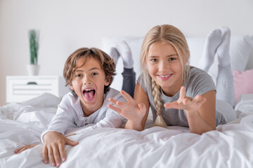 Schooler age brother and sister lying in bed and having fun at the morning. Childhood relatives...