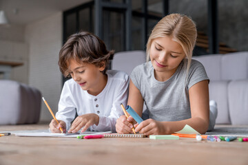 Two school age kids doing their homework on floor at home. Brother and sister siblings children drawing together, preparing for school lesson. Homeschool concept.