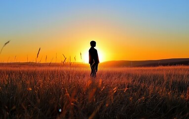 Fototapeta premium A silhouette of a person standing in a field as the sun sets, evoking a sense of self-reflection and inner peace, with a soft glow on the horizon and a calm