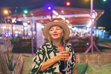 Obraz premium Female tourist on summer vacation drinking cocktail at night at beach bar