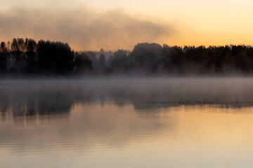 Obraz premium Blurred landscape with a lake in the morning fog, fog trailing over the lake