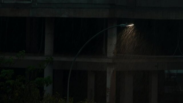 Heavy coming down in the evening with a street light in the fore ground and a Building under construction in the background dimly lit 