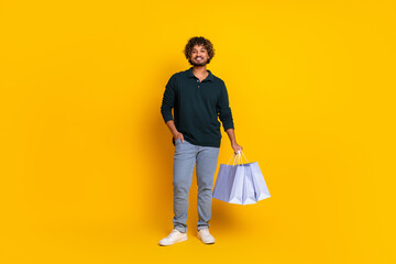 Happy young man holding shopping bags standing against vibrant yellow background for retail promotion