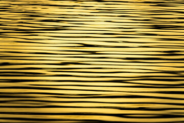 Obraz premium The image is of a body of water with ripples and waves. The water appears to be a golden color, giving the scene a warm and peaceful atmosphere. The ripples and waves create a sense of movement