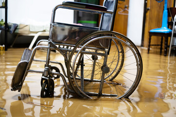 A wheelchair is sitting in a flooded room. The chair is in the middle of the room and is surrounded by water. The chair is tilted and he is in a state of disrepair. Scene is one of chaos