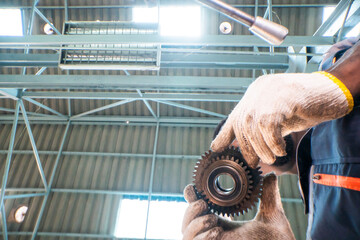 skilled worker inspects an industrial gear while holding it carefully with protective gloves. The...