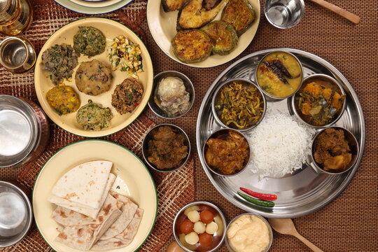 Bengali style thali spread verity cuisine hilsa fish vegetable beef mutton egg curry fry vorta mashed chicken liver sweet yogurt side dish served on rustic metal tin stainless steel plate small bowls