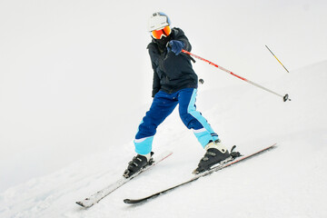 Young man learning to ski on a snowy slope having fun point finger to at camera while slowing down on snowy slope isolated