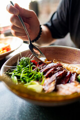 Close-up of a hand holding a spoon over a plate of gourmet food, showcasing vibrant colors and textures. Perfect for culinary, dining, and lifestyle themes.