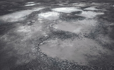 Puddles on the road after rainfall. The road is full of potholes. The road surface has been damaged. Erosion street from flooding.