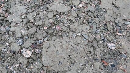 a close-up view of a rough, uneven surface that appears to be a patch of concrete or asphalt. The surface is made up of various small stones and gravel embedded in a grayish matrix, giving it a coarse