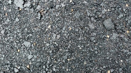 a close-up view of an asphalt surface. The texture is rough and uneven, with small stones and gravel embedded in the dark, tar-like material