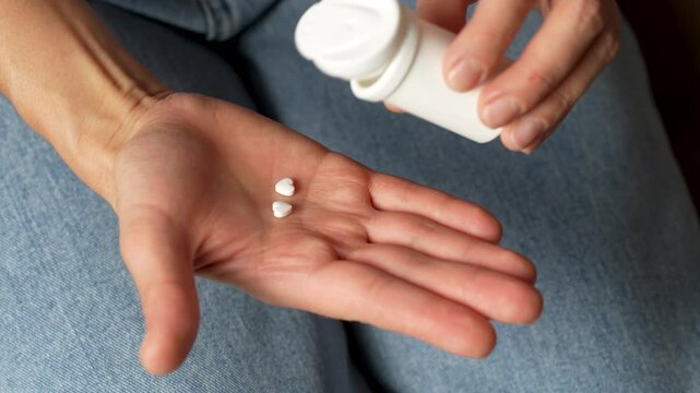 Woman taking heart shaped cardiac pills from bottle, close-up