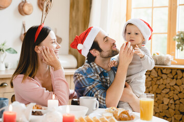 Happy New Year and Merry Christmas! Young family of three parents with toddler kid child celebrating winter holidays together, having dinner breakfast at home kitchen table