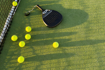 Padel racket and padel ball on a green court in the sunset