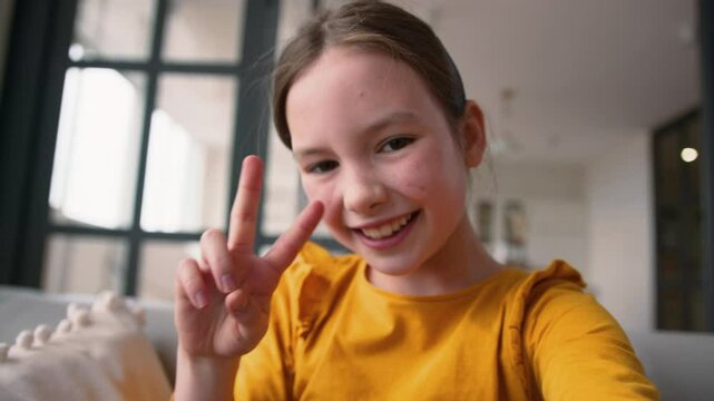 Playful Caucasian little girl child happy daughter making selfie photo on device smiling schoolgirl grimacing kid type screen display mobile phone at home point of view smartphone webcam photography
