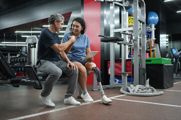 A trainer person with prosthetic leg,holding digital tablet,doing fist bump with senior client after finished discussing workout program design,concept of health,exercise,athlete