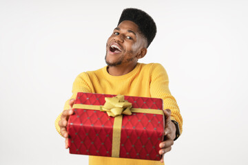 Fototapeta premium Happy excited dark skin guy african american man dressed casual red knitted sweater smiling holding present gift box isolated white color background. Holiday concept