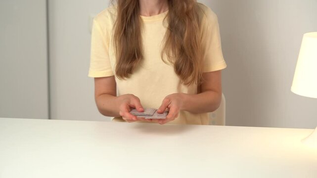 A young woman shuffles the cards before dealing them while sitting at the table. Concept of board games and pastime