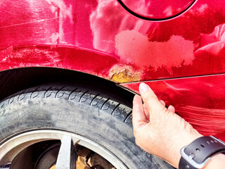 A person is directing their finger toward a rusty place on the car, indicating it