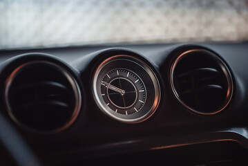 Car interior clock showing 21:50. Close-up image of round clock and two air ducts on both sides of it.
