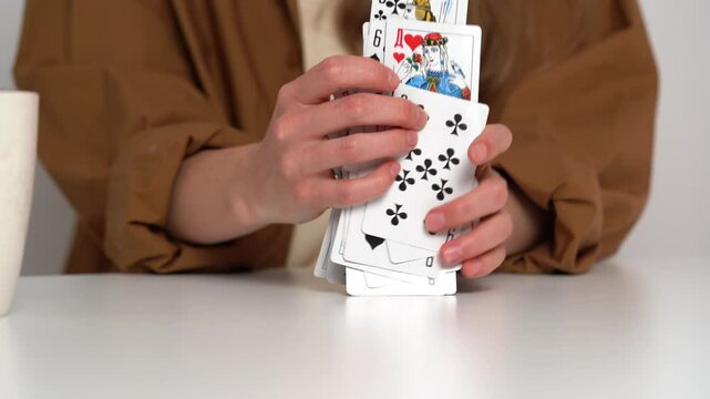 The hands of a young woman collect and shuffle cards from the table, distributing them for the next game. Entertainment concept, having fun, card board games