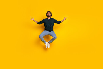 Obraz premium Young man in a black shirt and jeans jumping joyfully against a bright yellow background on a casual friday