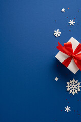 White vertical gift box with a striking red ribbon surrounded by decorative snowflakes on a blue...